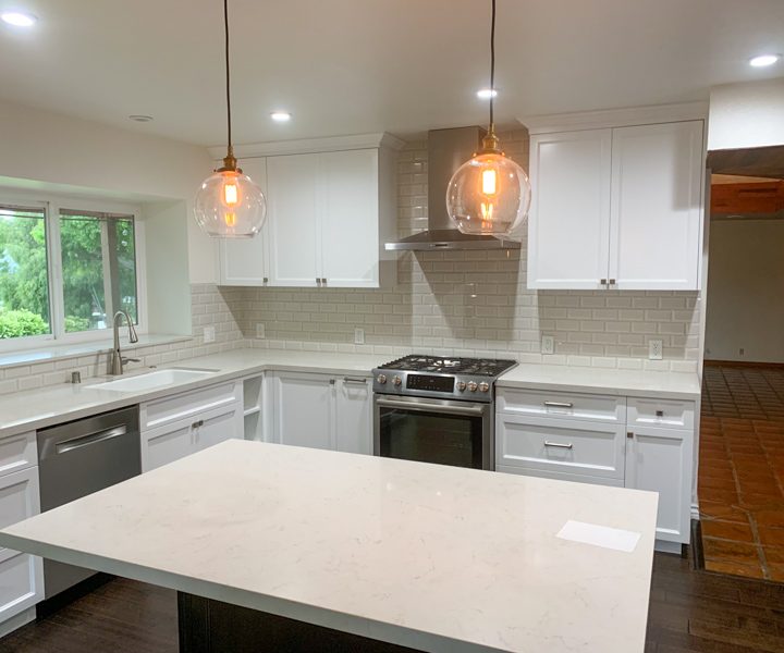 a kitchen with two hanging lights, a center island with marble countertop and white painted kitchen cabinets