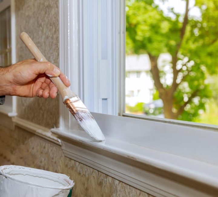 Hand with paintbrush painting a window trim white house interior