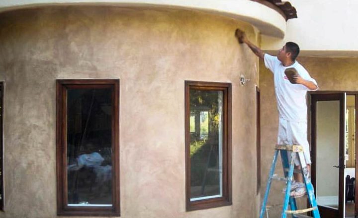 a worker painted a stucco wall finish of the house being renovated