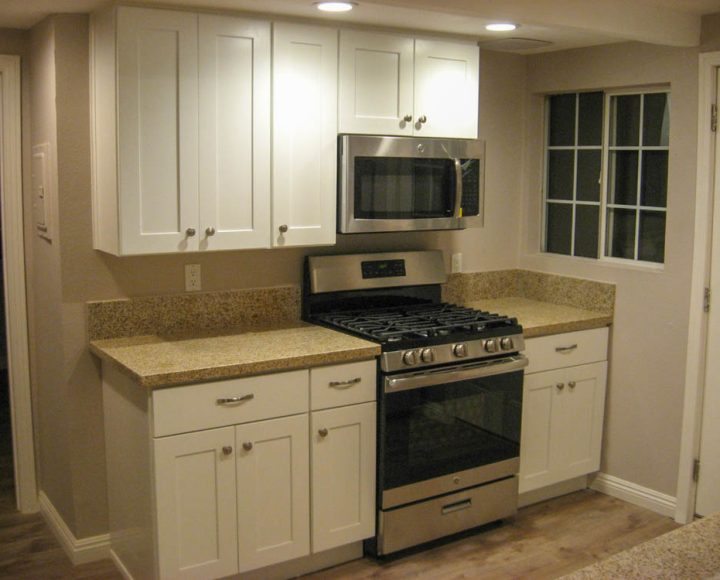a kitchen with range, microwave, granite countertop, and newly painted cabinets and walls